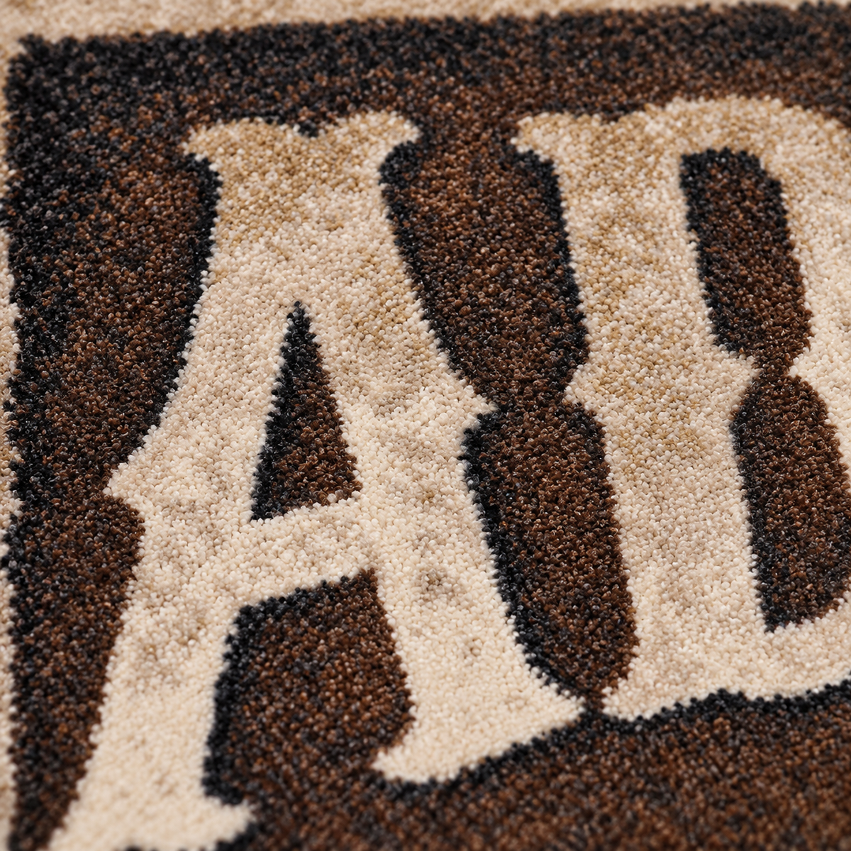 Close-up of a textured rug featuring large cream-colored letters outlined in dark brown and black.