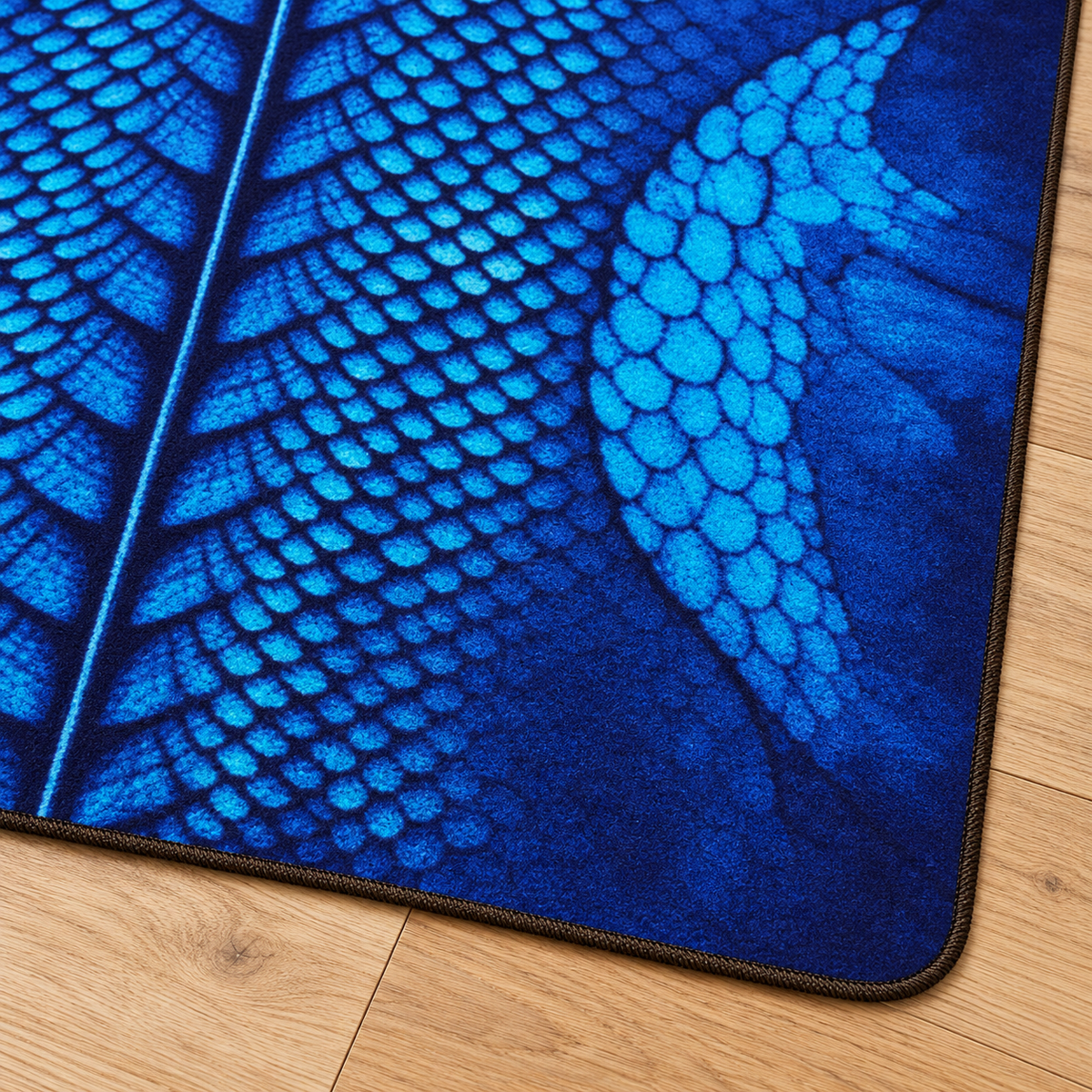 A close-up of a blue textured rug with a detailed reptile or dragon scale pattern, shown on a light brown wooden floor.