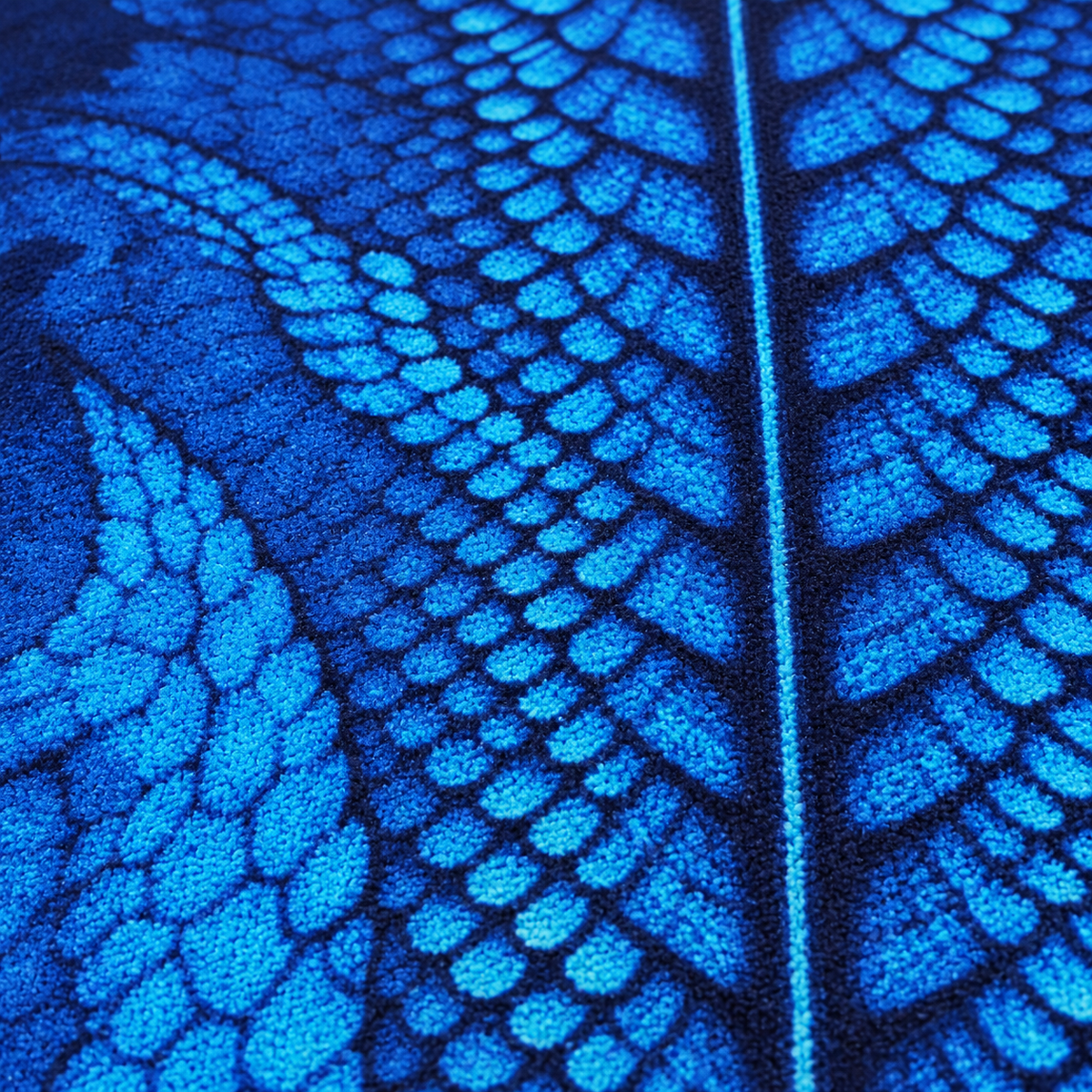 A close-up of a textured fabric featuring a detailed blue and black leaf pattern with a central vein design.