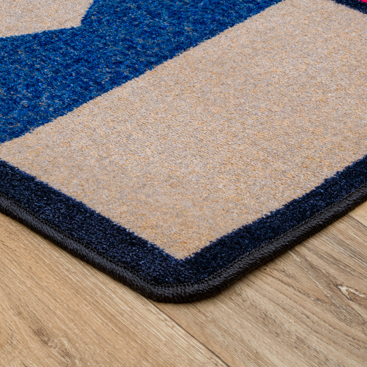 Close-up of a rug corner on a wood floor, showing a beige field with a thick dark navy border and a blue geometric section.