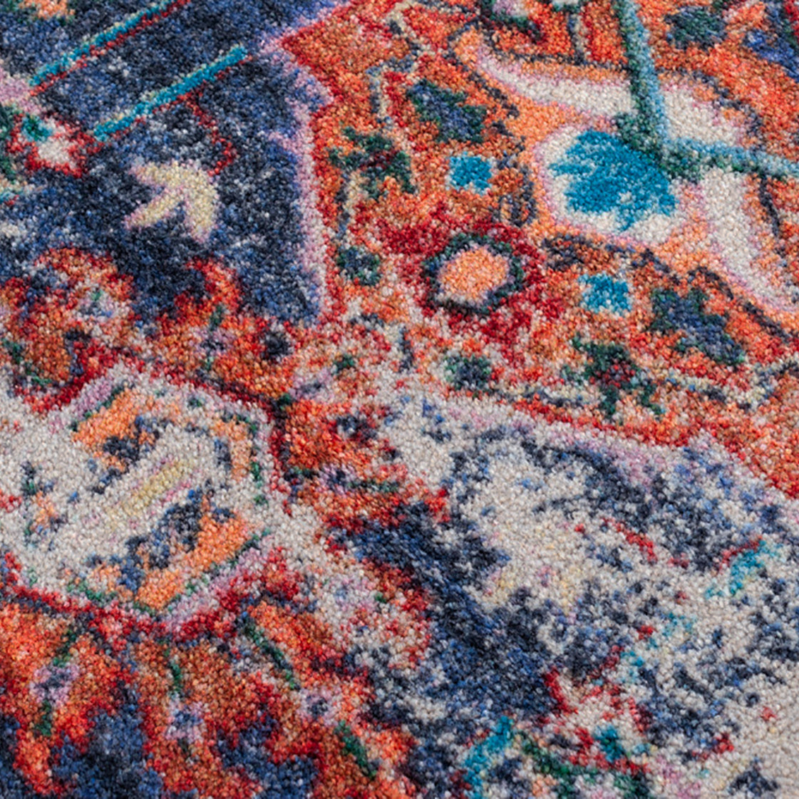 Daydream area rug: a close-up of a ttextured area rug with a distressed, vintage-style pattern featuring a mix of rust red, navy blue, teal, cream, and orange.