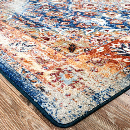 A close-up of an area rug corner on a hardwood floor, featuring a distressed traditional pattern in blue, rust orange, beige, and brown.
