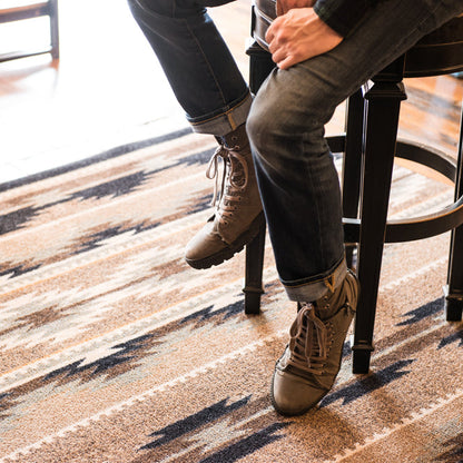 Field Notes area rug: person sitting on a stool wearing brown boots and dark jeans on a patterned rug.