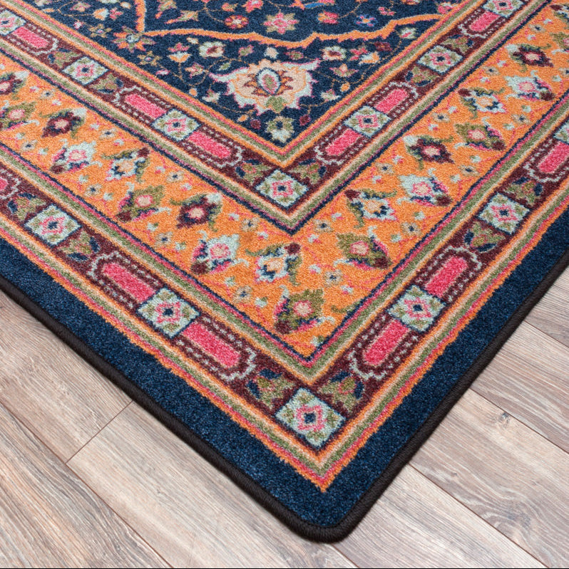 Full House area rug: a close-up of a traditional patterned area rug with a navy blue field, orange borders, and pink and green floral motifs, shown on a light wood floor.