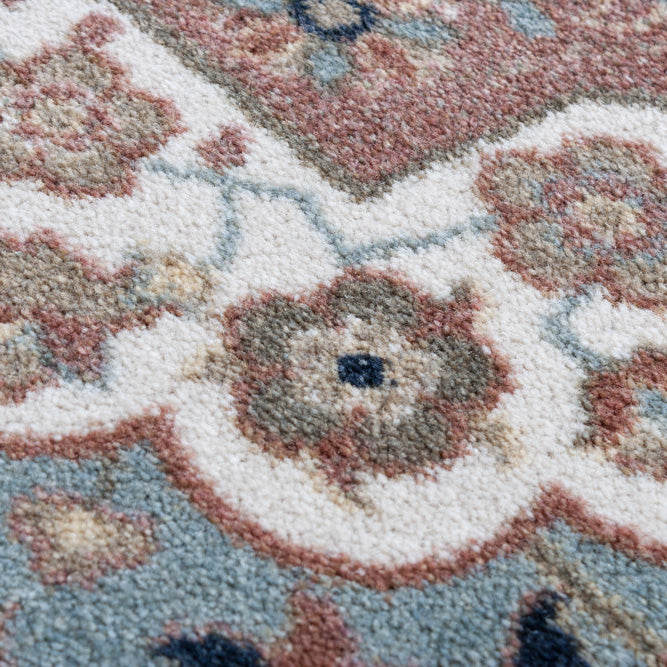 Close-up of a patterned area rug with floral motifs in cream, dusty blue, terracotta, taupe, and dark navy.