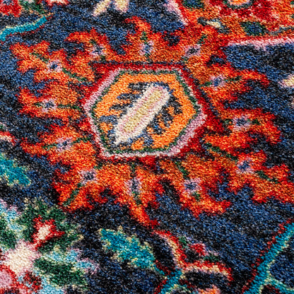 Good Company area rug: close-up of a ttextured area rug with a traditional floral or medallion pattern in navy blue, rust red, orange, teal, cream, and black.
