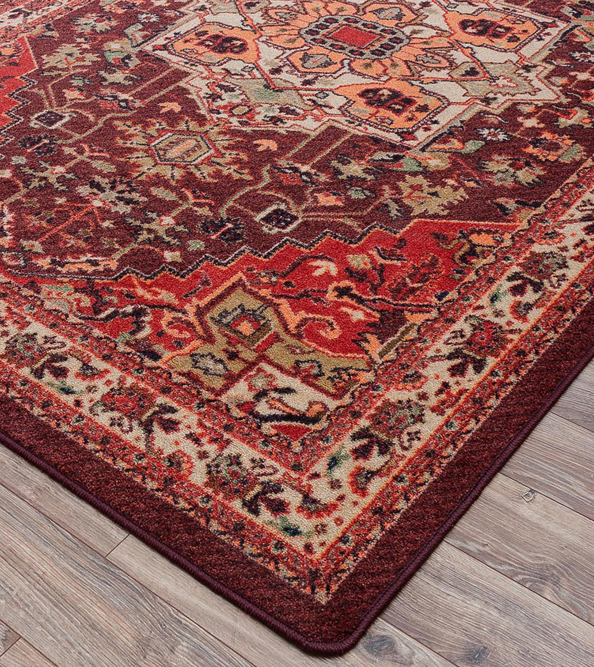 Hot Streak area rug: a traditional oriental area rug with an intricate floral and geometric pattern in deep red, burgundy, beige, and orange, shown laid out on a gray wood plank floor.