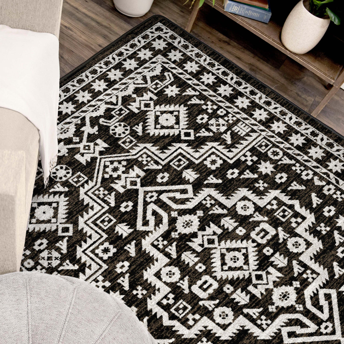 A brown and white area rug with a detailed geometric tribal pattern, shown in a styled living room setting on a dark wood floor.