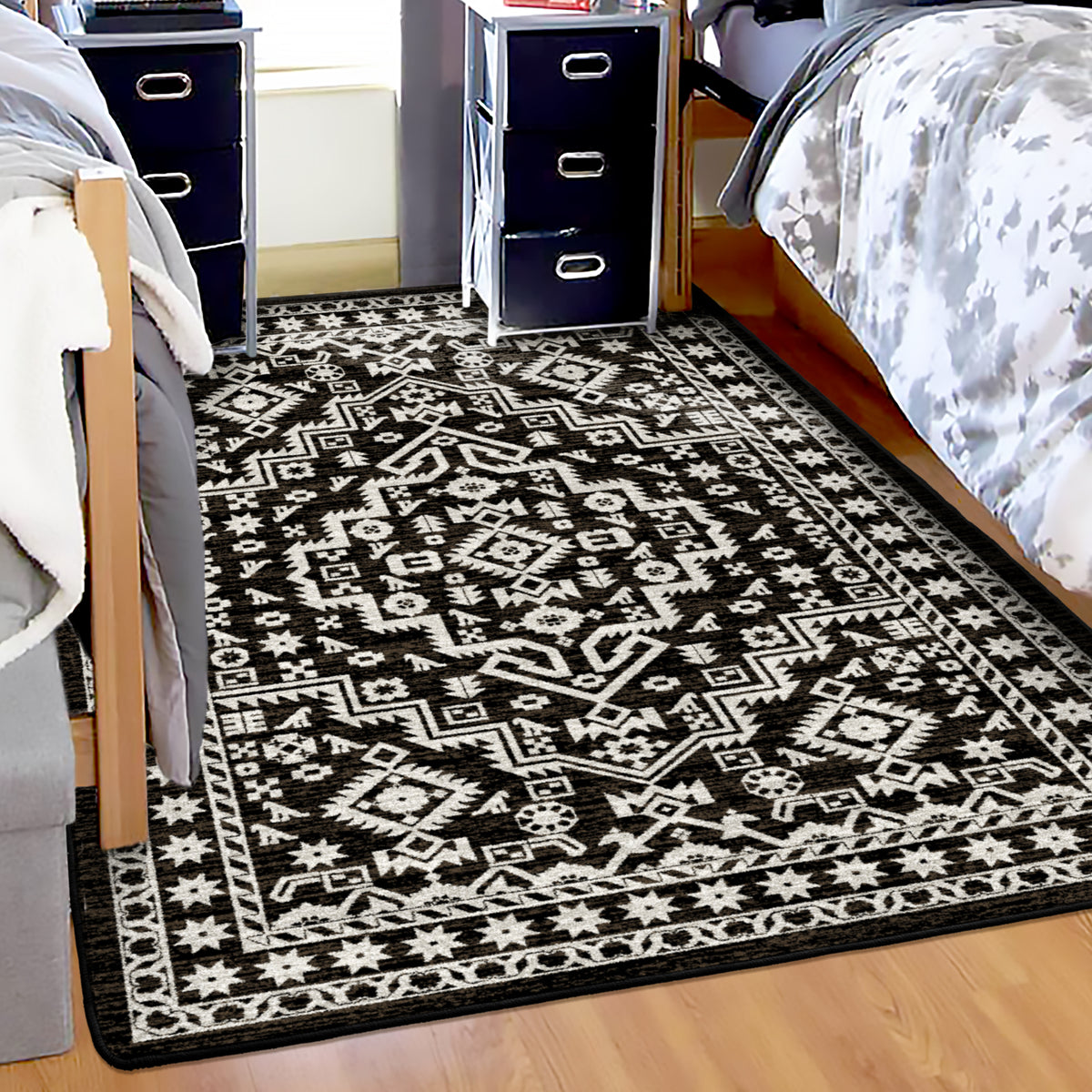 A brown and white patterned area rug with a geometric tribal design, shown on a light wood floor in a bedroom setting between two beds and nightstands.