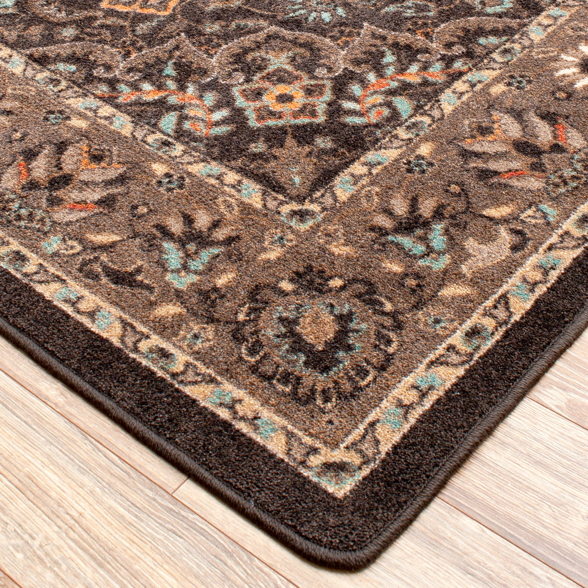 House Special area rug: a close-up corner view of a traditional area rug with a dark brown base, beige borders, and teal and orange floral accents, shown on a light wood floor.