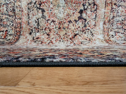 Close-up of the underside of a patterned area rug resting on a light wood floor, showing the dark woven border and multicolor rug fibers.