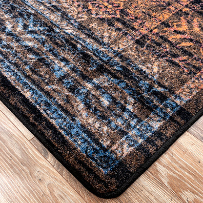 Last Call area rug: a close-up of a patterned area rug corner on a light wood floor, showing a distressed design in black, brown, blue, and orange tones.