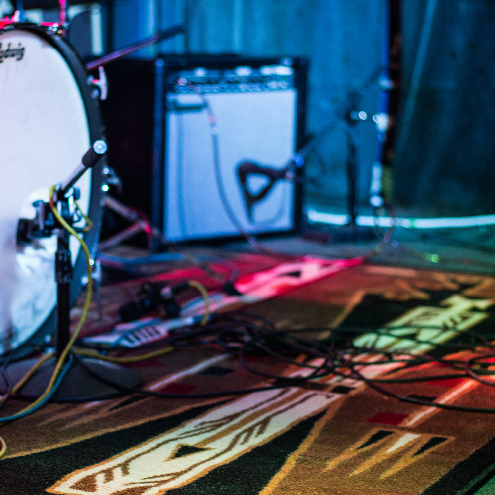 Red drum set with cables on a stage with a guitar amplifier in the background on top of the long game area rug.