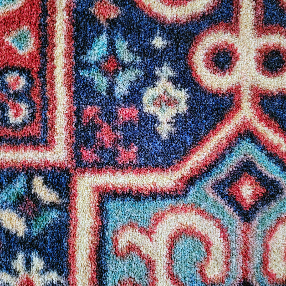 Close-up of a textured area rug with a traditional geometric and floral pattern in navy blue, cream, red, and light blue.