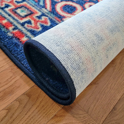 A close-up of a rolled area rug showing its cream-colored underside and dark navy blue backing, placed on a light brown wooden floor next to the patterned top side.