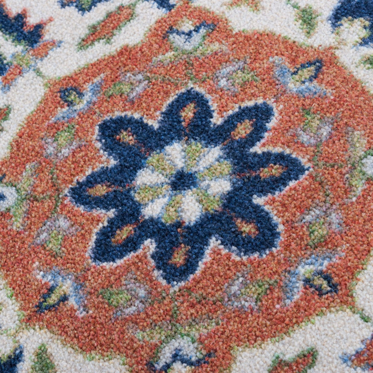 Night Garden area rug: close-up of a ttextured area rug featuring a traditional medallion pattern with a prominent orange center, a dark blue floral motif, and a cream background.