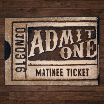 A rectangular mat designed to look like a vintage 'Admit One Matinee Ticket' with distressed beige and dark brown tones, placed on a dark wood floor.