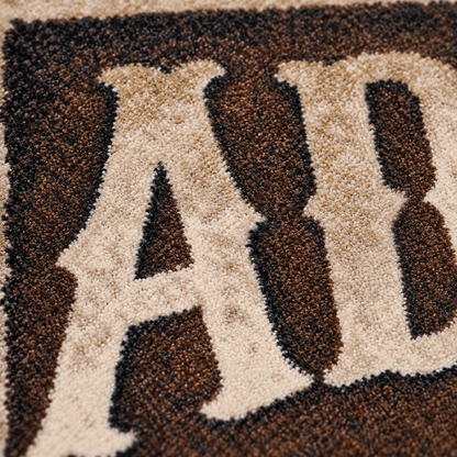Close-up of a textured rug featuring large cream-colored letters outlined in dark brown and black.
