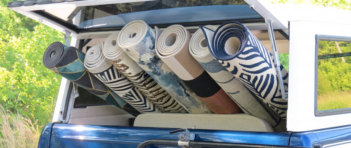 Several rolled area rugs with various patterns, including zebra print and blue abstract designs, stacked in the open back of a blue pickup truck outdoors.
