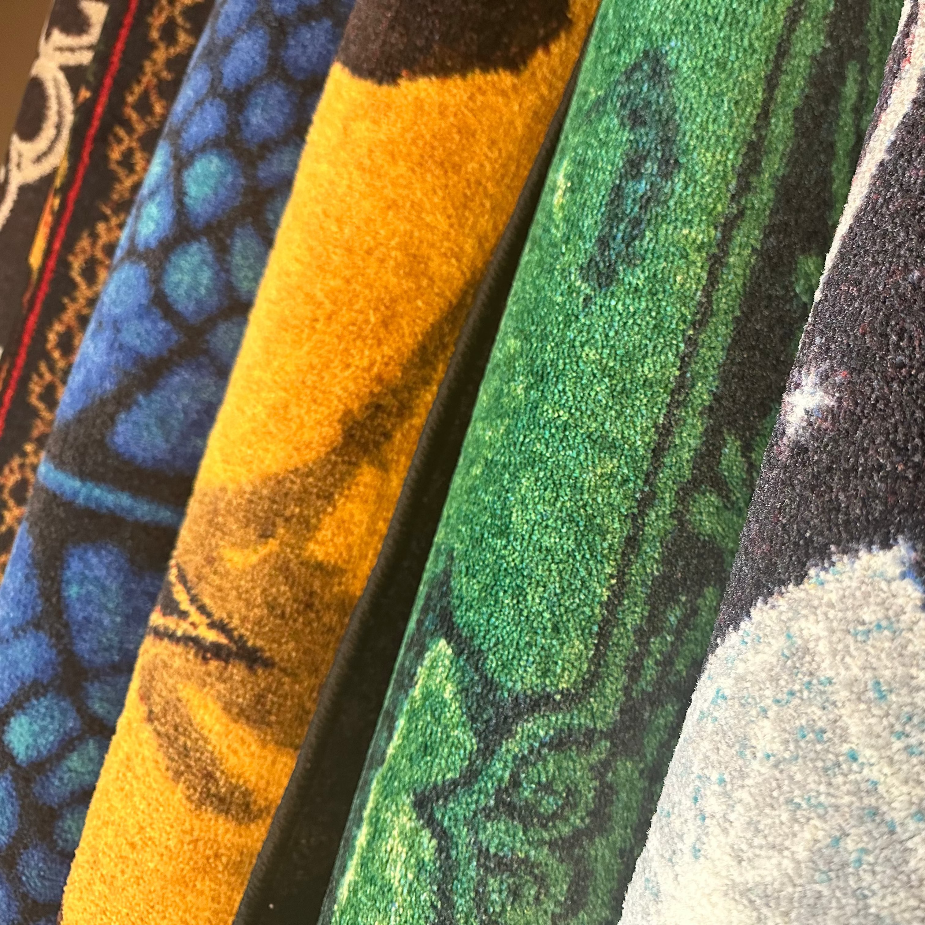 Close-up of several patterned fabric or carpet samples standing vertically, showing bold designs in blue, mustard yellow, green, black, and white.