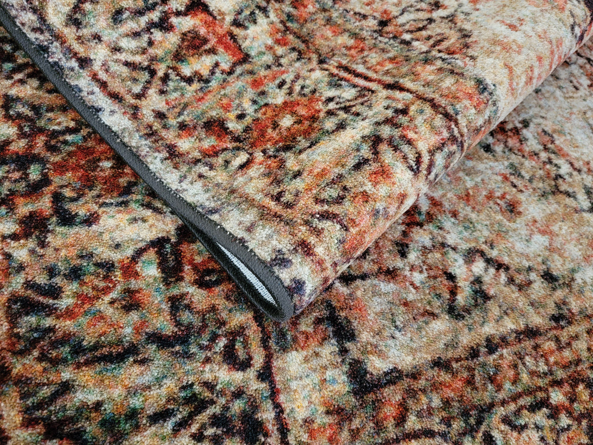 A close-up of a folded vintage-style area rug showing its detailed multicolor floral and geometric pattern in beige, rust orange, black, and muted green tones.