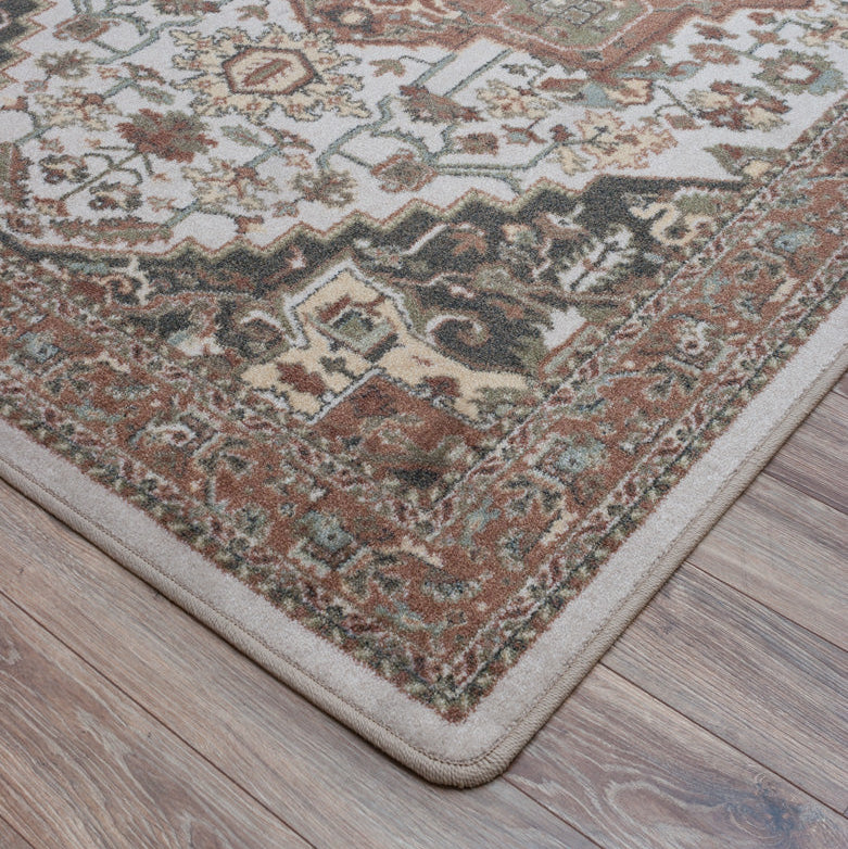 A close-up corner view of a traditional patterned area rug with a beige border, shown on a light brown wood floor.